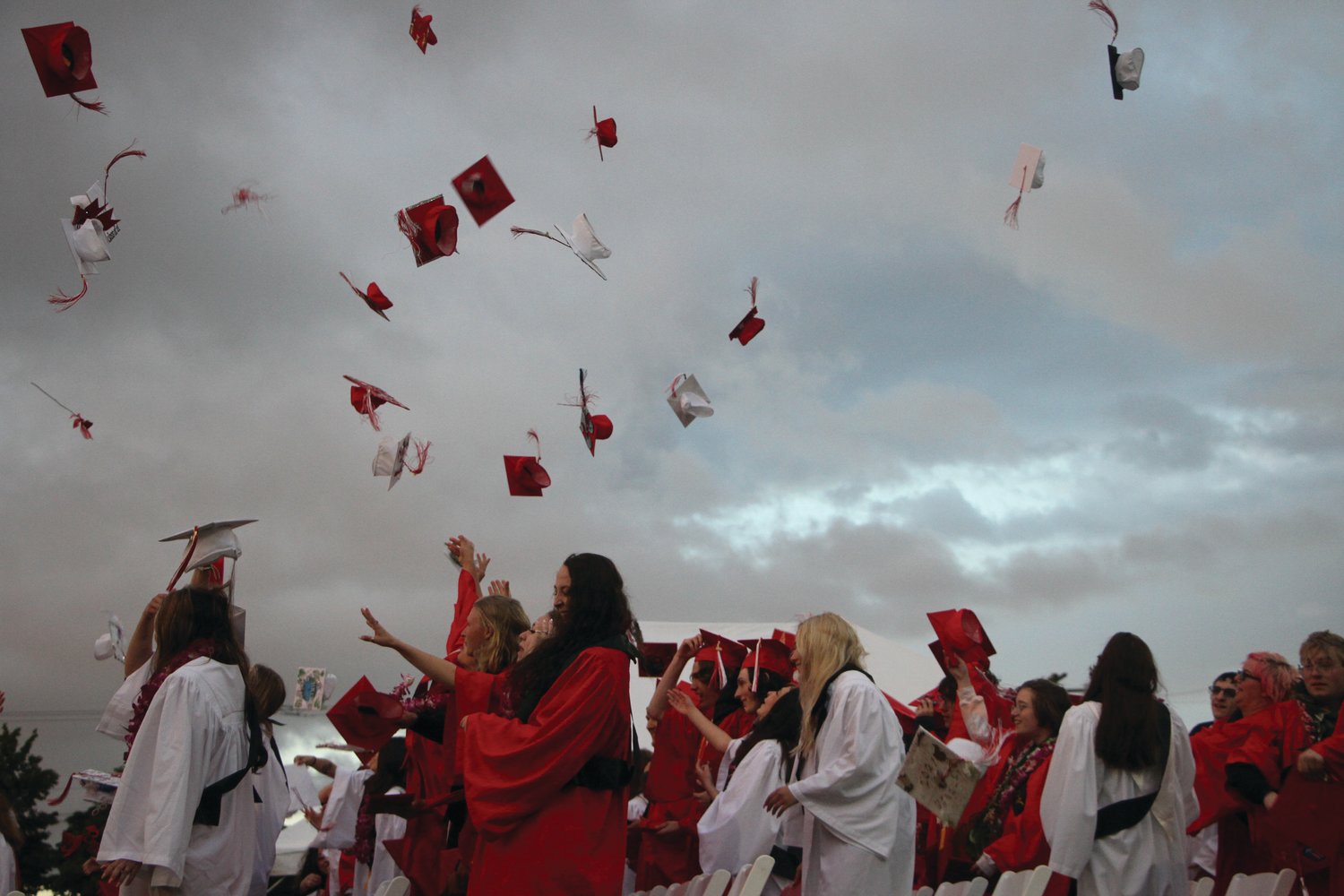 Graduates toss their caps into the setting sun and watch them fall back to earth like red and white raindrops.