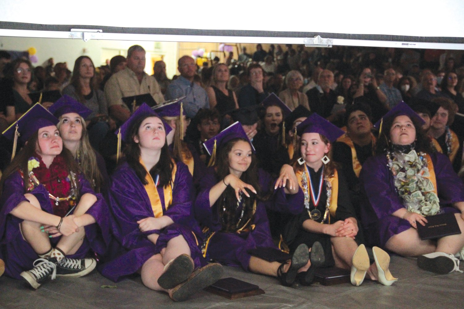 Quilcene’s graduating class sits on the floor of the gym to watch a slideshow during the commencement ceremony.